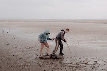 Two kids poke a stick into the mud of a dried reservoir.