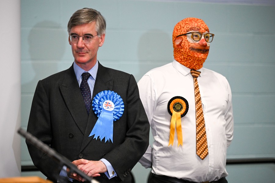 Two politicians stand side by side, one of them wearing a full head covering decorated with an image of baked beans.