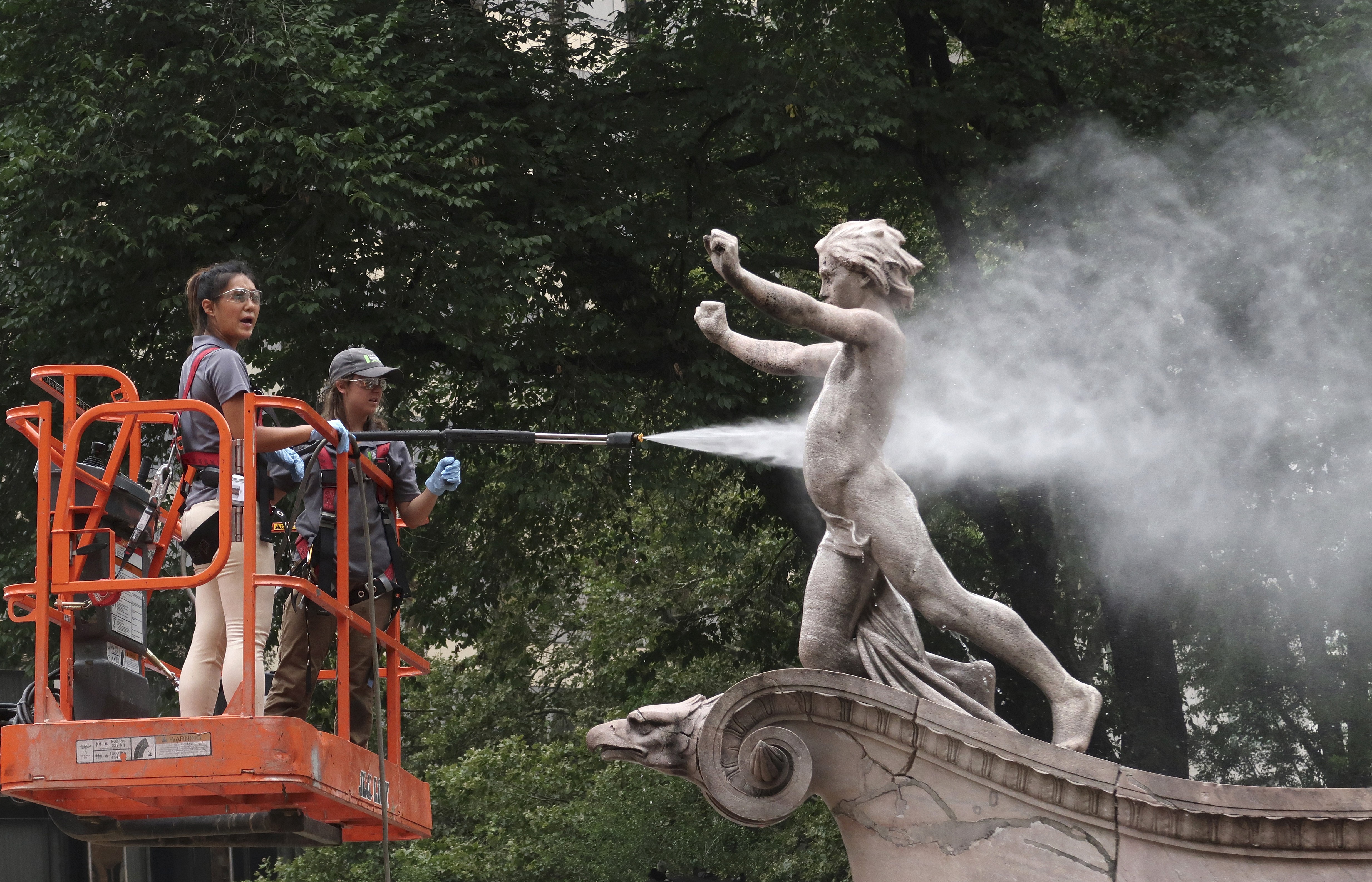Two maintenance workers spray water on a statue in a park.