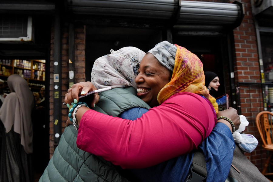 Two women embrace while standing on a sidewalk.