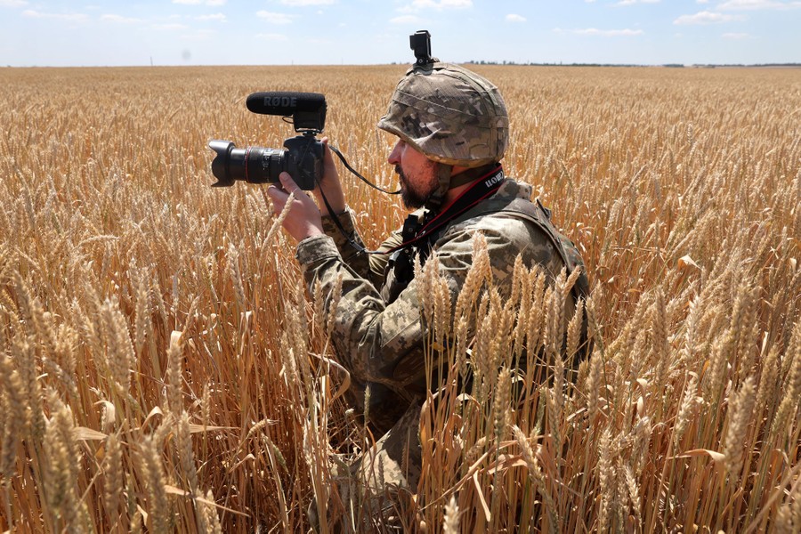 A Ukrainian military journalist holds a camera up while filming in a wheat field.