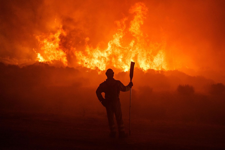 A firefighter stands before a large wildfire in the distance.