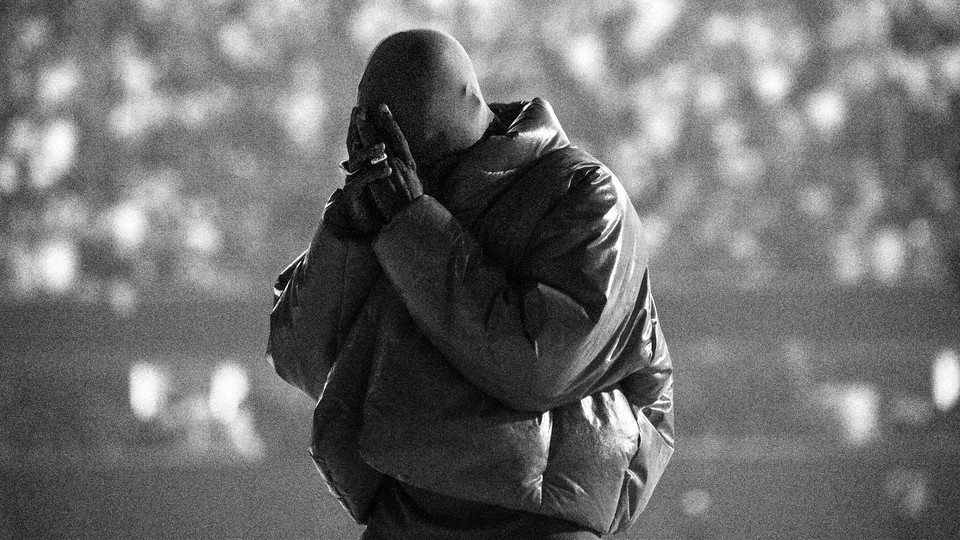 A black-and-white image of Kanye West, with his head bowed and his hands over his face, at a 'Donda' listening event last month