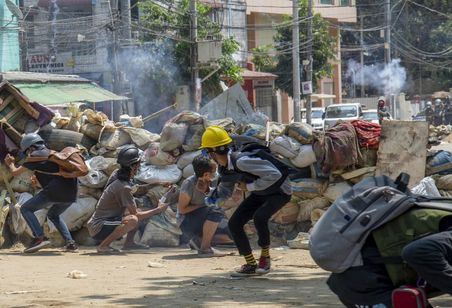 Protesters run from a barricade in a street, as police advance in the distance.