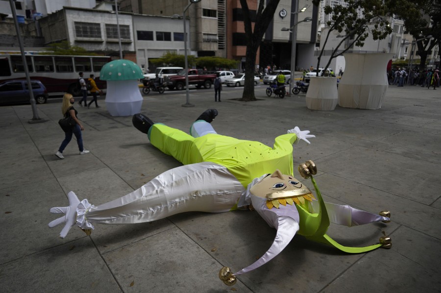A large inflatable harlequin doll lies on its back in a plaza.