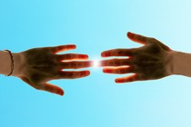 Two hands, raised to the sky, touching as the sun beams down between them