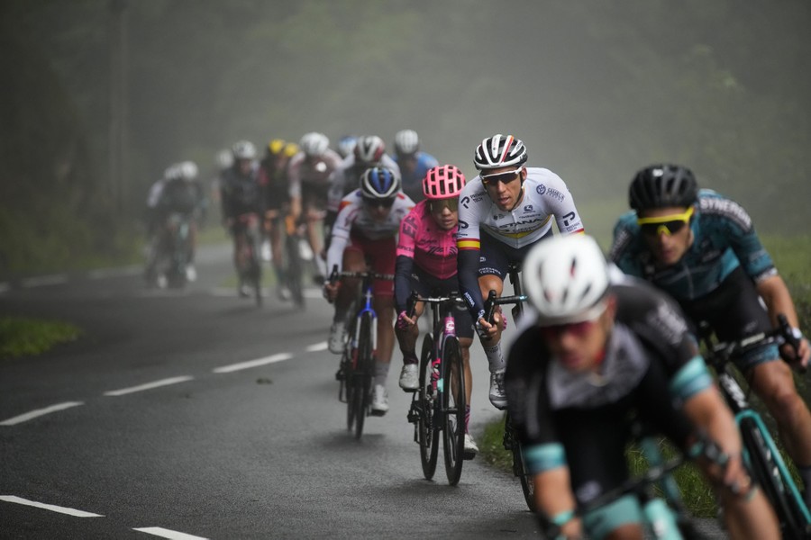 A group of cyclists race down a twisty mountain road in fog.