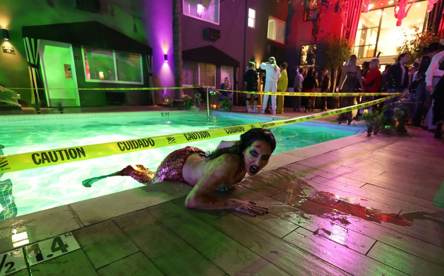 A person dressed as a zombie mermaid crawls from a pool.