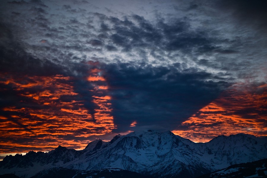 A sunrise view of a tall mountain that casts shadows onto low clouds