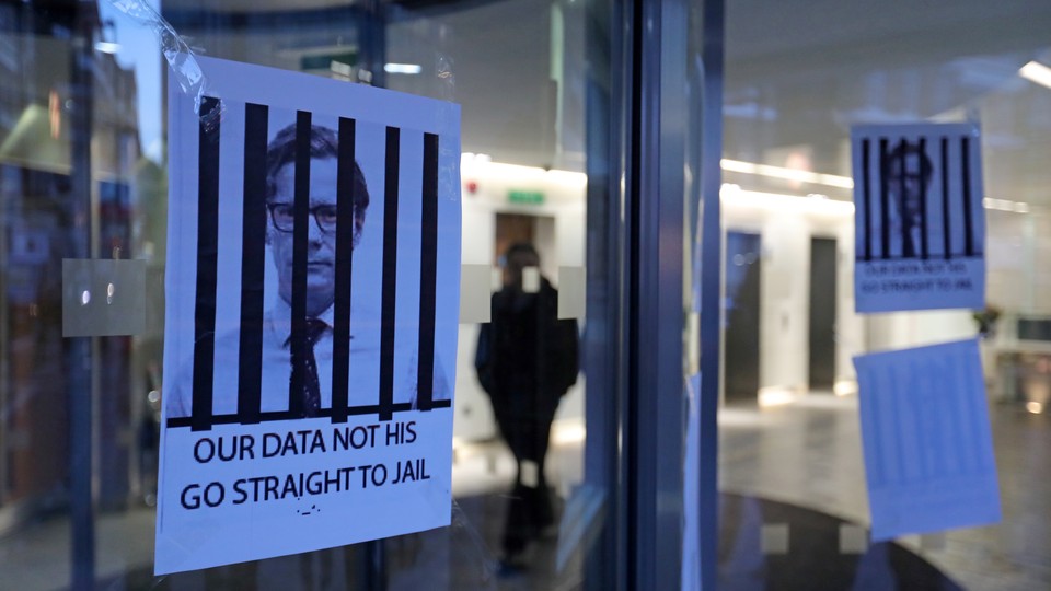 Posters hang on a glass door depicting the Alexander Nix behind bars with the text, "Our Data Not His. Go Straight to Jail."