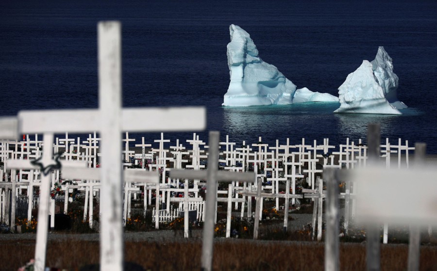 An iceberg floats offshore, near a graveyard.