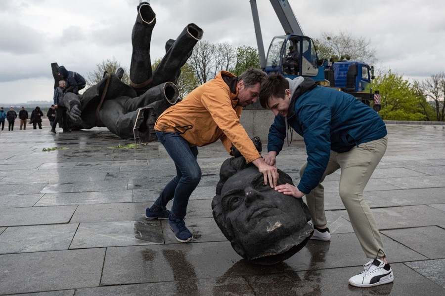 Two men move the removed head of a statue.