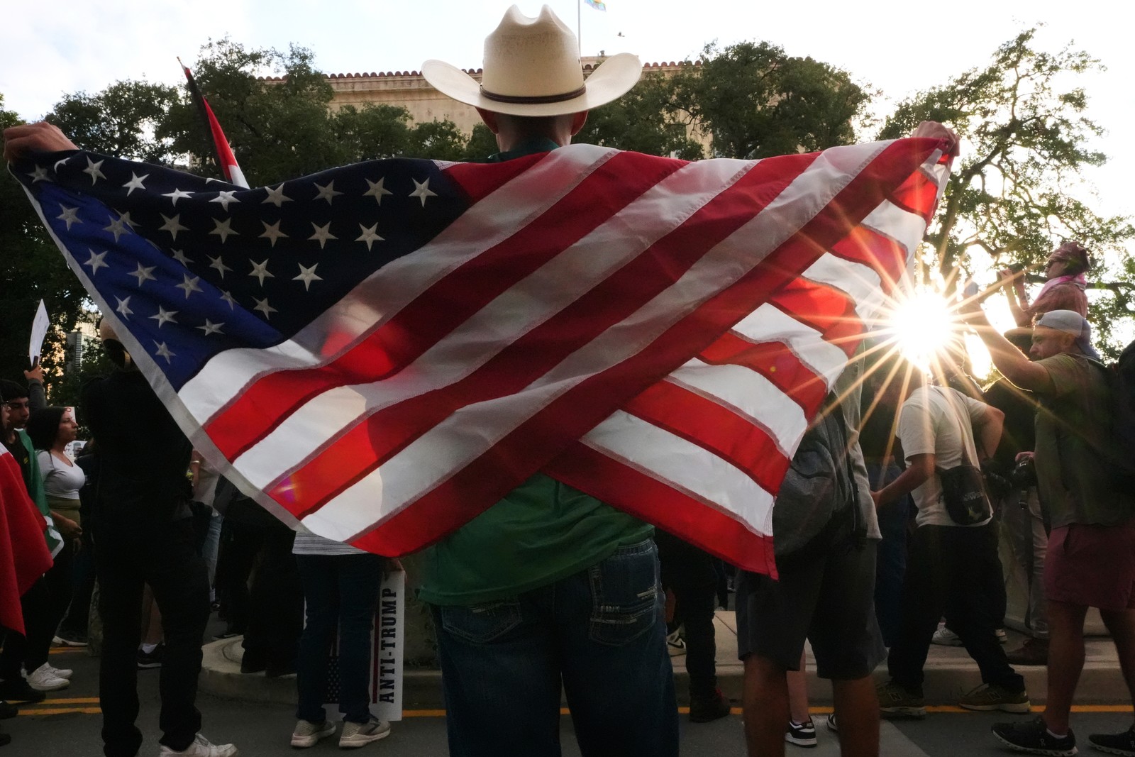 A protester stands near others, arms outstretched, with an American flag draped over their shoulders.