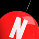 A red balloon with a white "N," with a needle pointing at it, against a black background