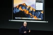 Tim Cook stands in front of a projected image of an Apple laptop.