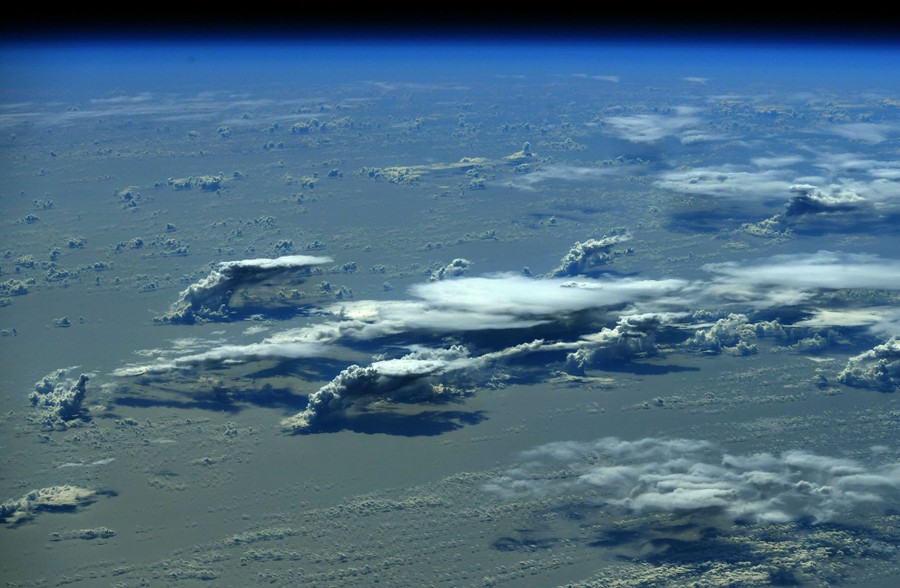 Clouds are seen from above, rising from the ocean's surface to the upper atmosphere.
