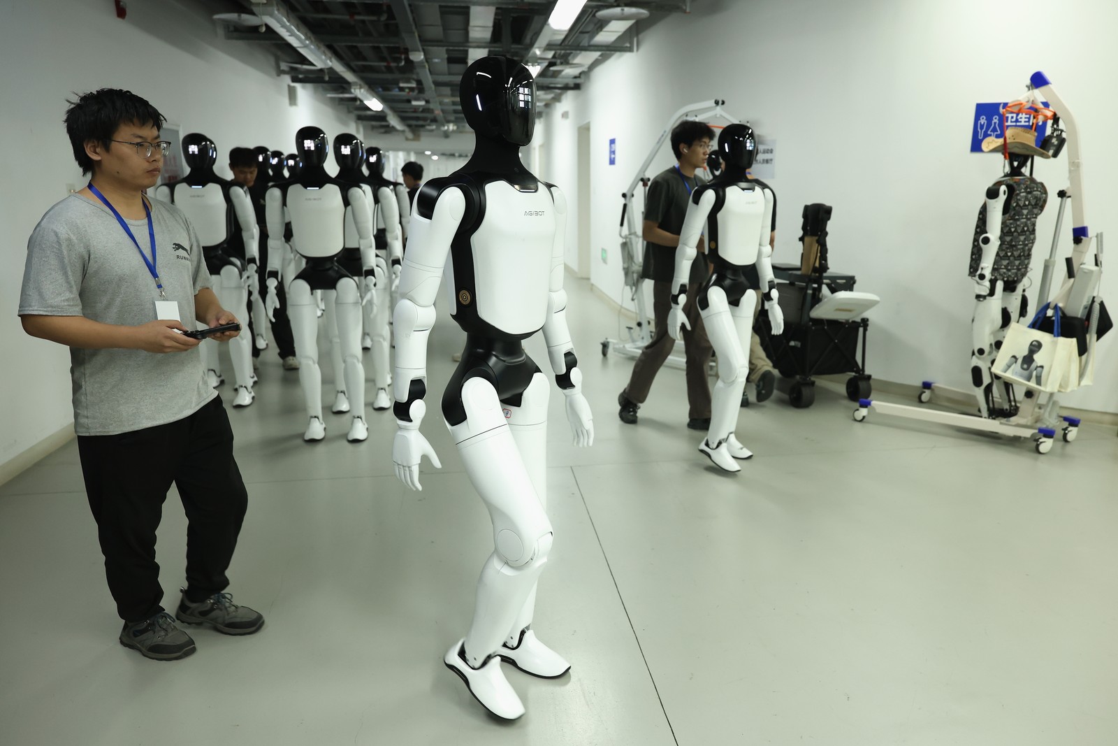 Human technicians guide several humanoid robots in a hallway.