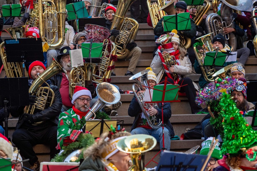 Many tuba players perform, wearing Christmas-y hats and coats.