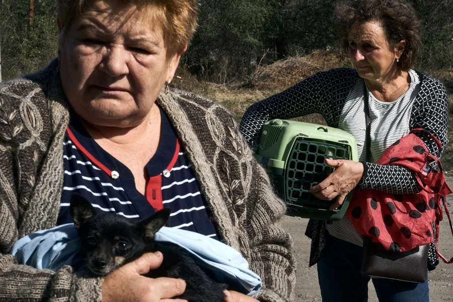 Two people carry their pets while waiting outside.
