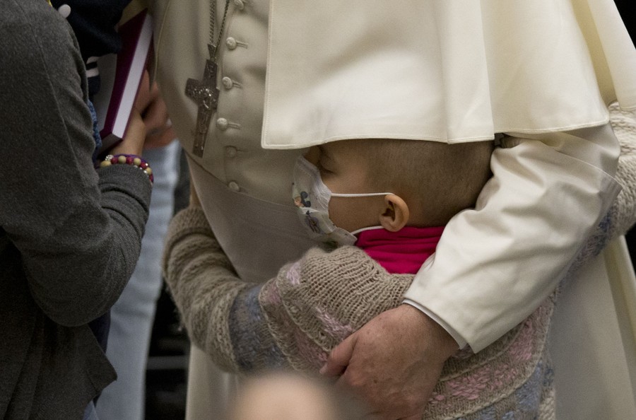 Pope Francis is hugged by a child wearing a protective mask.