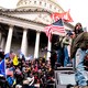Trump supporters stand and wave flags on the steps of the U.S. Capitol building.