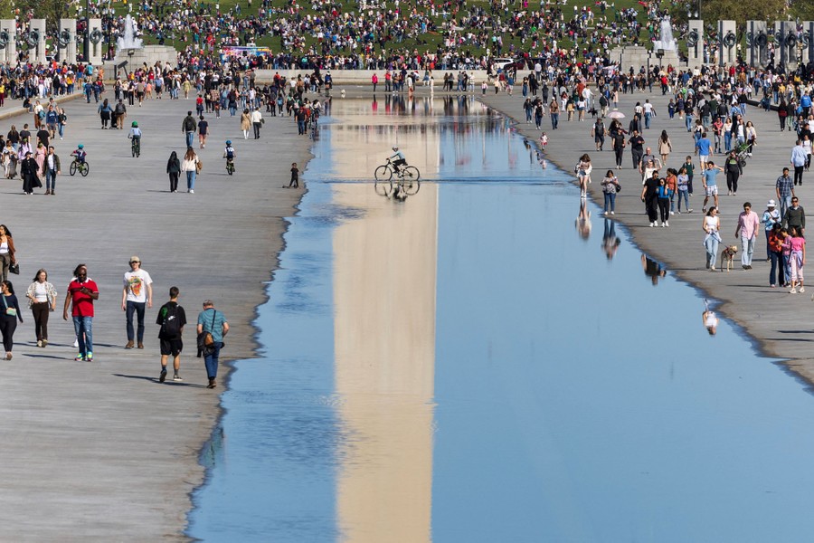 People walk, and one rides a bicycle, in a partially drained reflecting pool in Washington, D.C.