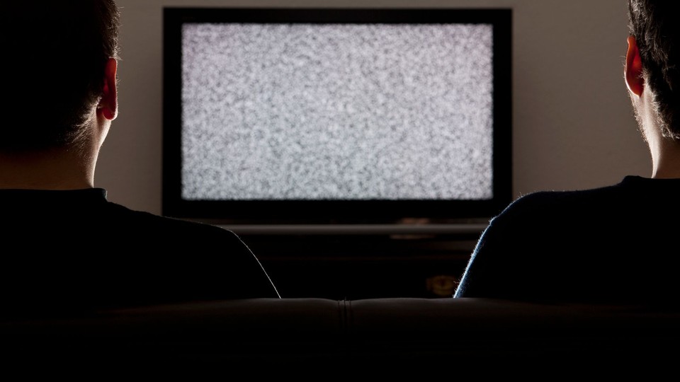 Two men watch static on a television screen
