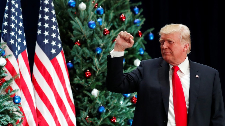President Trump makes a fist while standing in front of American flags and Christmas trees.