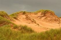 A sand dune with grass on it in the foreground and dark hurricane storm clouds in the background