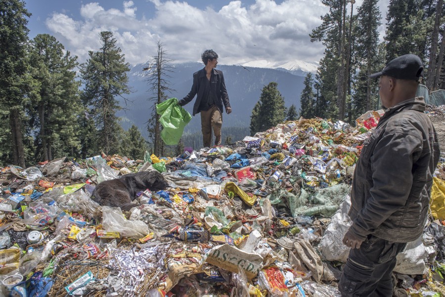 People walk on top of a hill of garbage in a mountainous area.