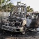 A burned shell of a car bearing World Central Kitchen logos sits along the side of a road as onlookers gather around it. The vehicle was damaged in an Israeli attack in Deir al-Balah, Gaza, on April 2, 2024. Seven staff members of the humanitarian organization, including Western nationals participating in food relief efforts and a Palestinian, were killed.