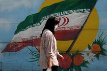 A woman walks in front of a mural of the Iranian flag