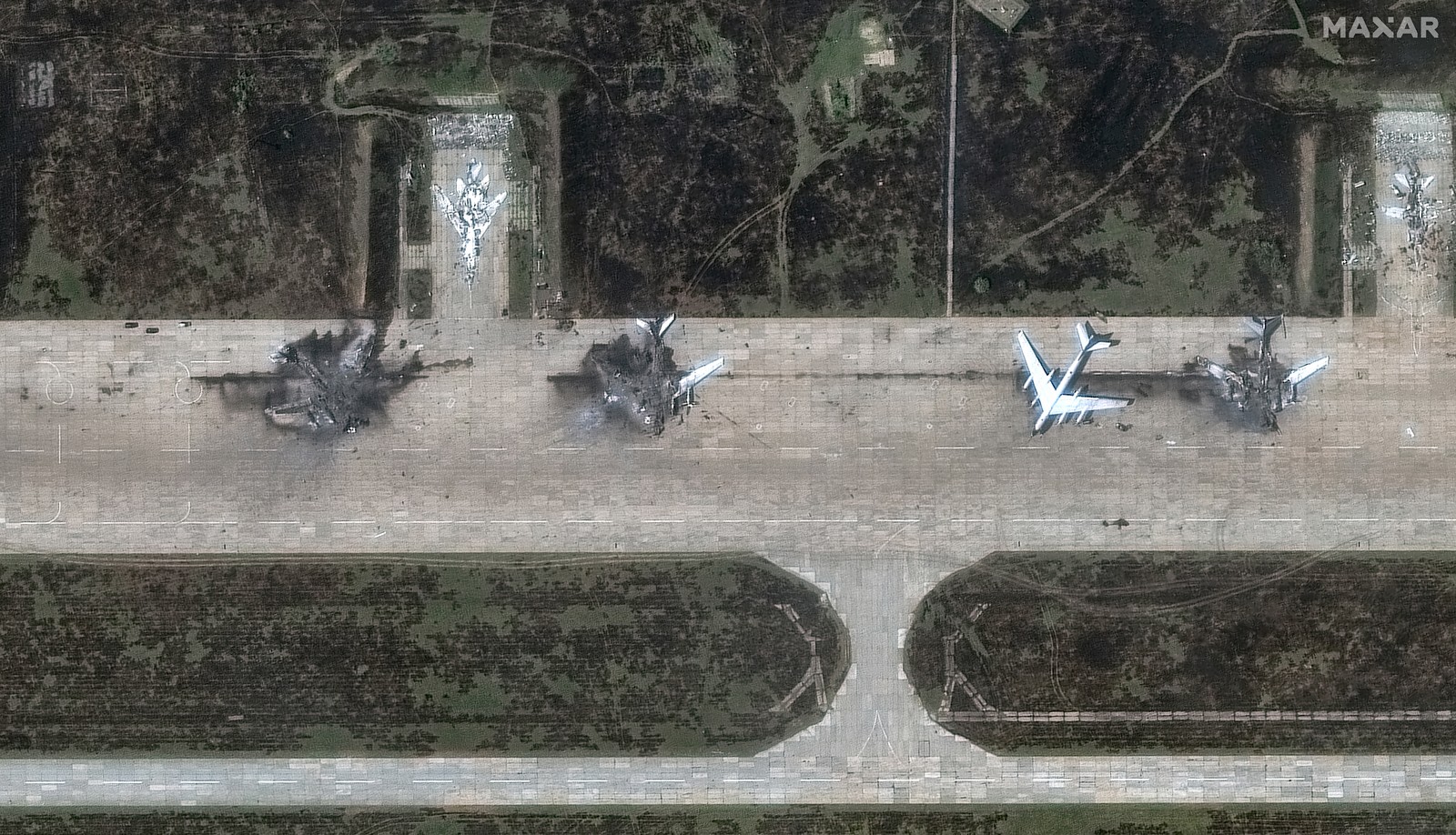 A satellite view of the charred remains of several large bomber aircraft, on an airfield