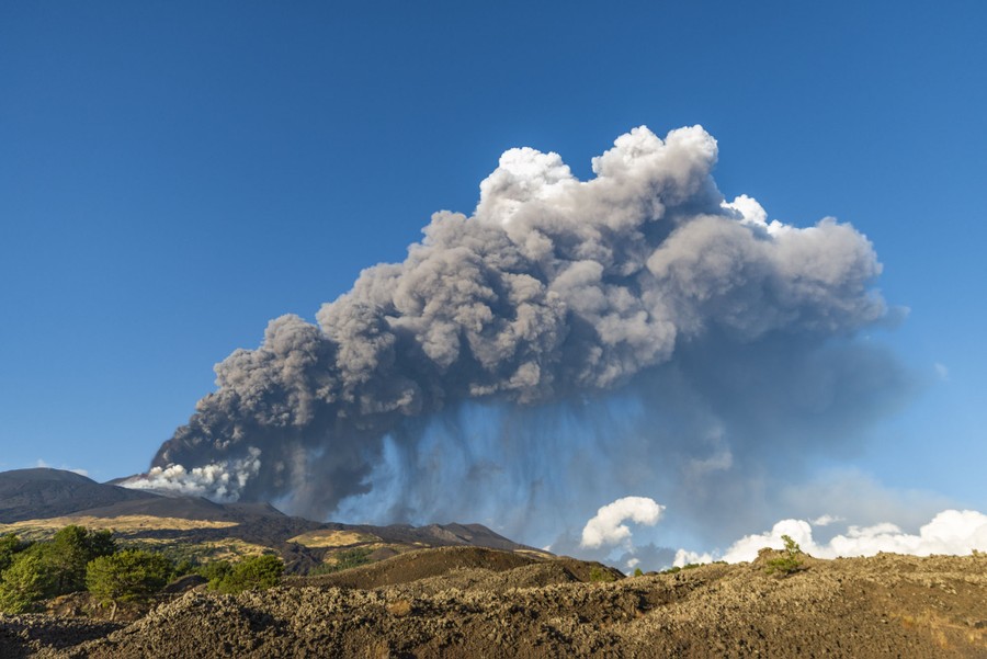 A plume of ash rises above a distant Mount Etna.