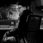 A black-and-white photo of Steve Albini in glasses and a hat, sitting in a recording studio