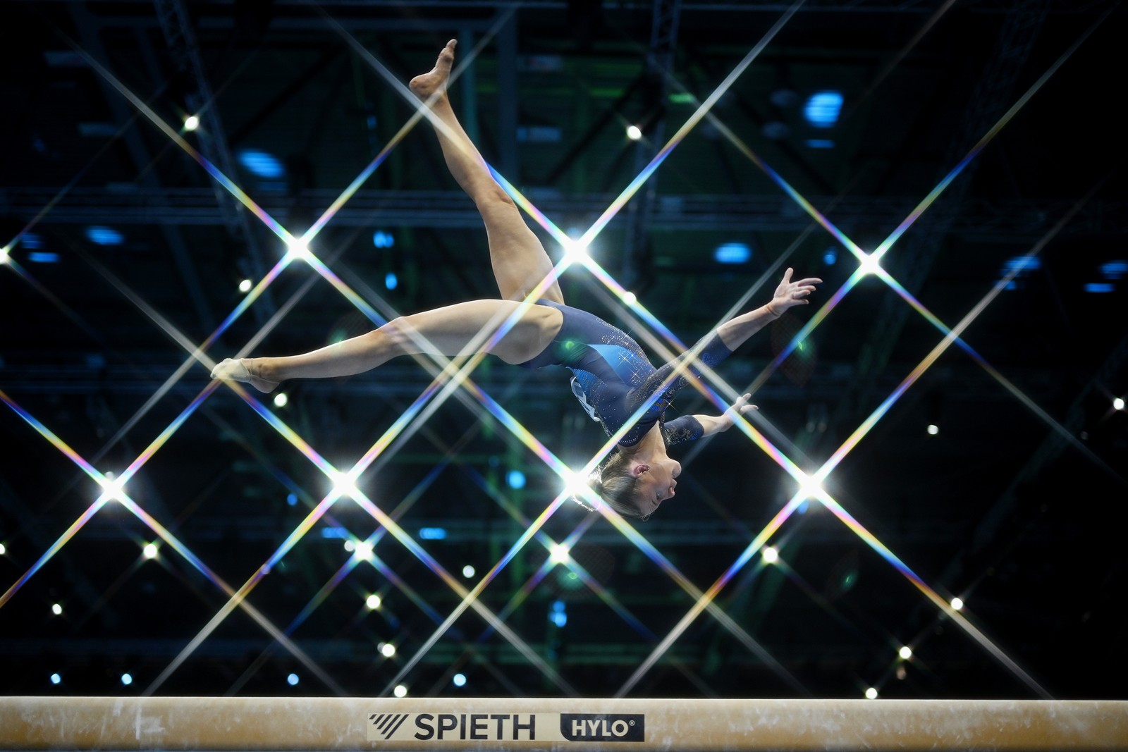 A gymnast flips in the air above a balance beam.