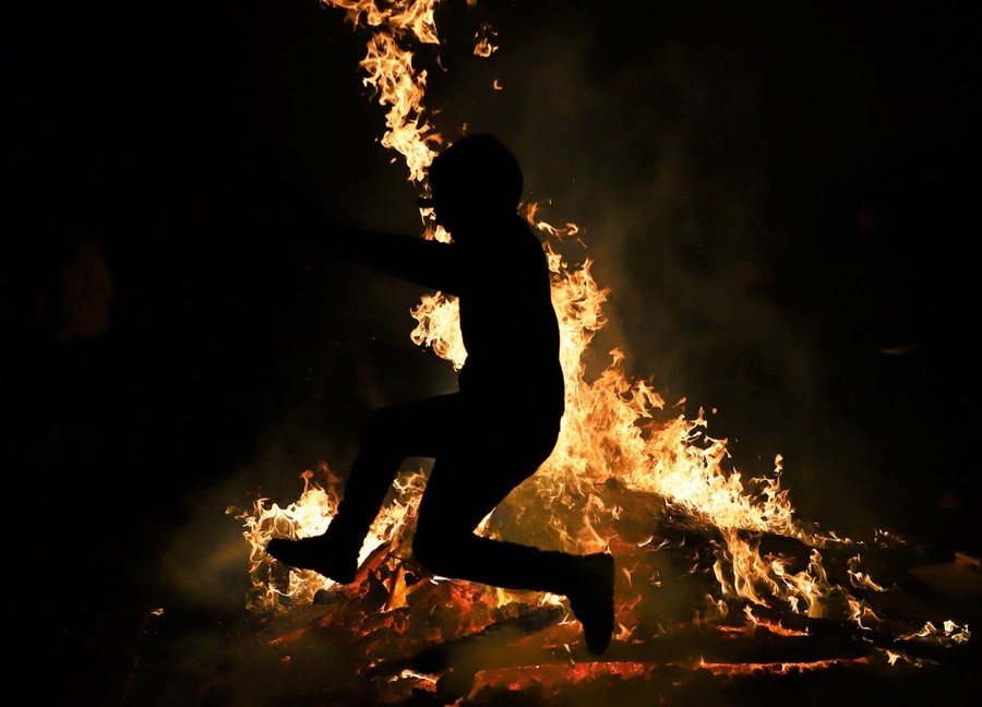 A person leaps over a large fire.