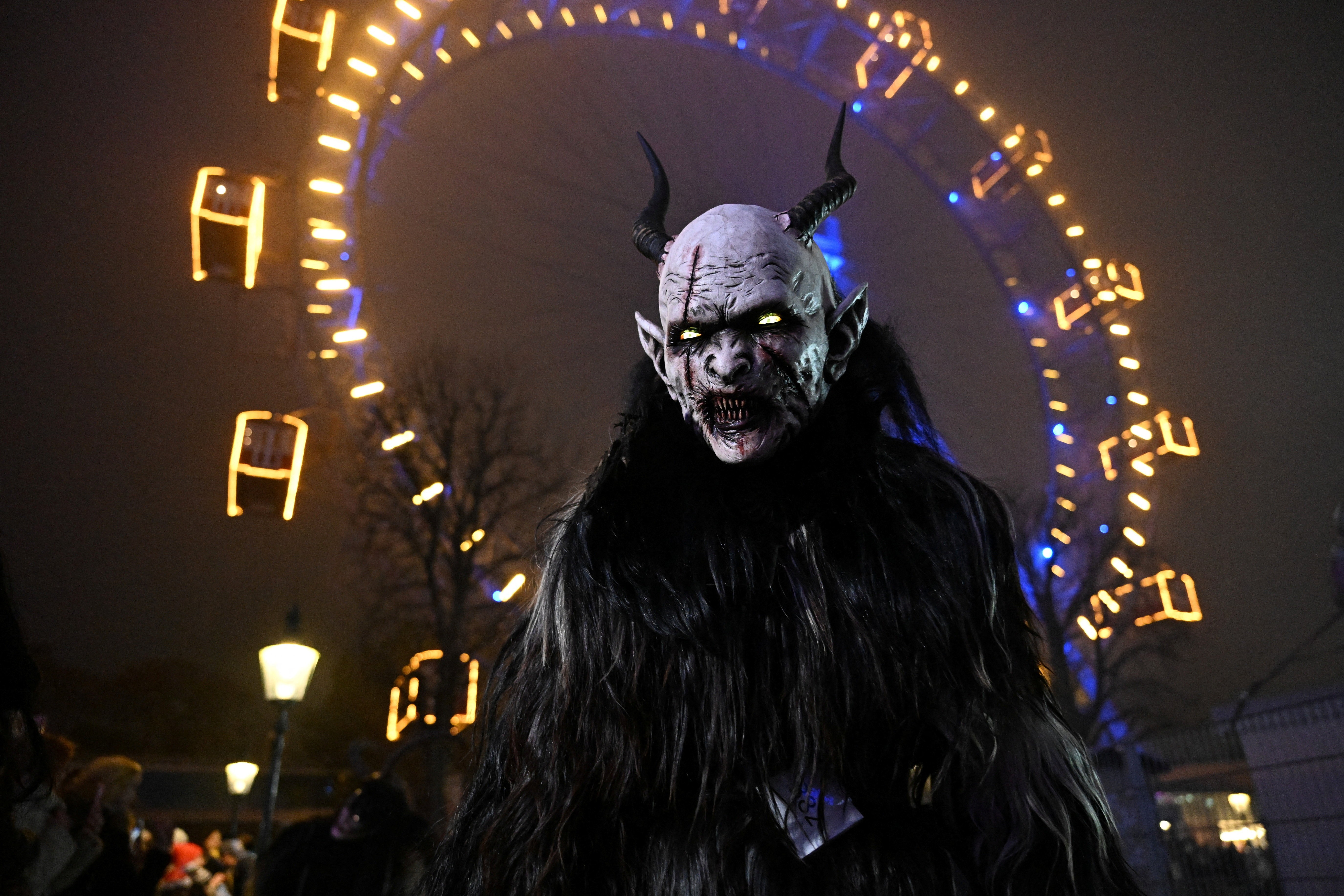 A close view of a person wearing a Krampus costume and mask, seen standing in front of a Ferris wheel