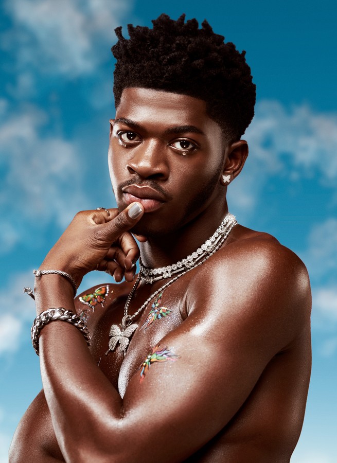 Lil Nas X shirtless in bedazzled jewelry against a blue sky