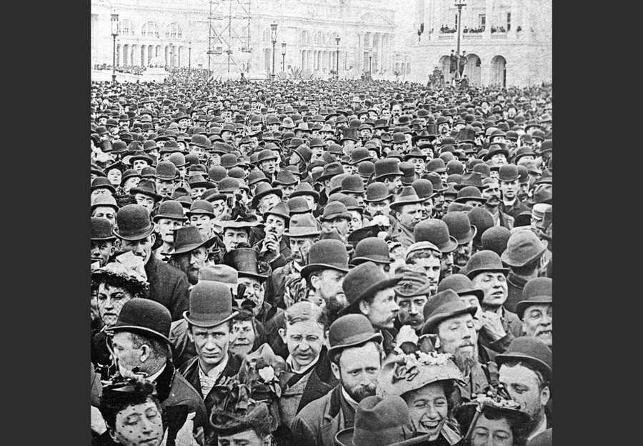 So many hats. A crowd of mostly men, almost all wearing hats, fills a wide open space in a fairground in 1893.