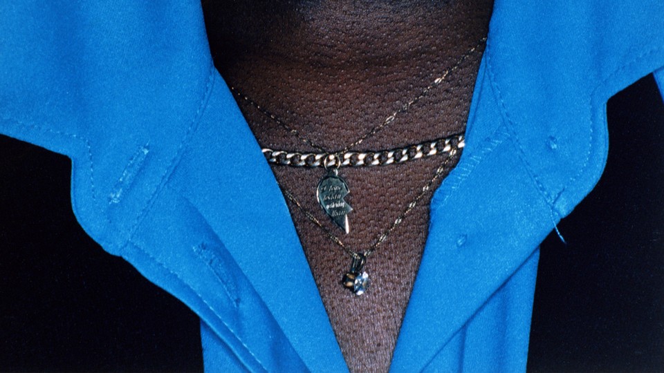 A close-up of an upper chest with a bright-blue shirt and three necklaces, including a gold chain and half a heart