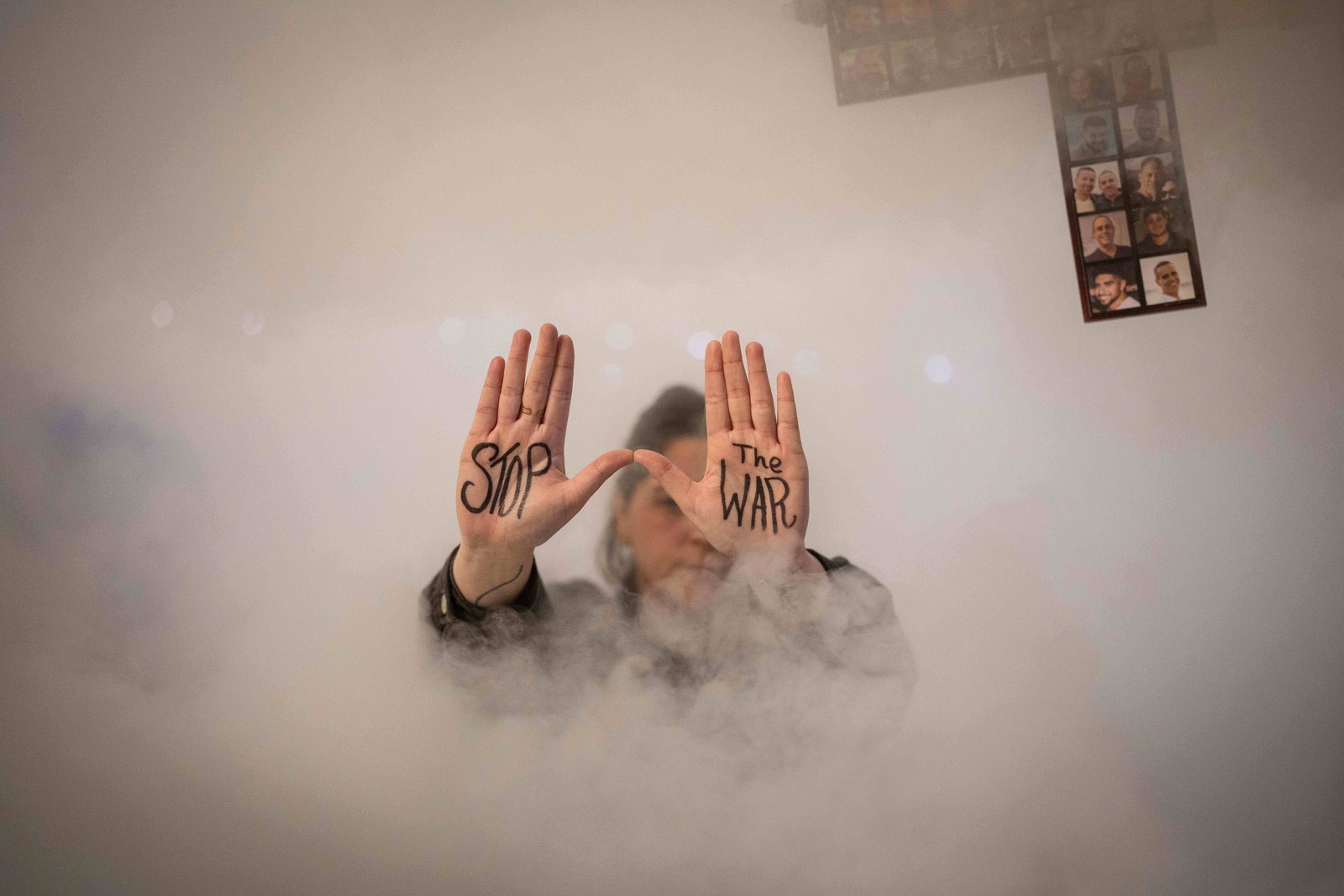 A protester, partially obscured in a cloud of smoke, shows the phrase “Stop the War” written on her palms during a demonstration.