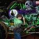 A young man stands beside a monster truck that features a skull on its side.