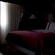 A young man sits on a hotel-room bed, alone, and looks out the window.
