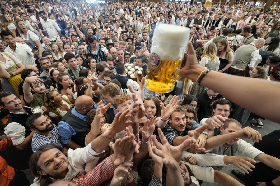 A large crowd fills a beer hall, with many near the front reaching up for a large glass of beer.