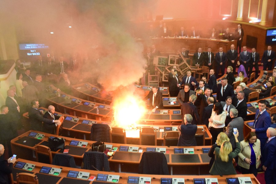 A small fire burns on a desk inside a parliamentary hall as politicians look on.