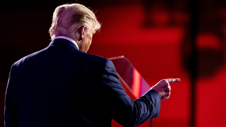 Former President Donald Trump stands with his back to the camera, pointing a finger to the right.