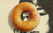 A black-and-white sketch of an Asian woman against a cream background. A sesame bagel is centered over her left eye.