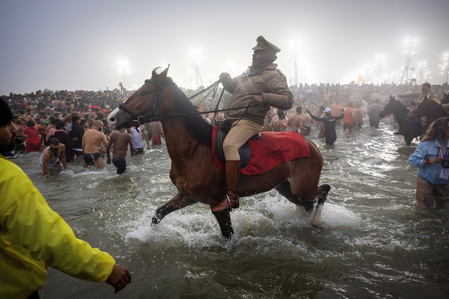 Police officers on horseback ride in shallow water, urging a crowd of worshippers back to the shore.