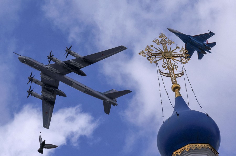 Two military aircraft fly low, overhead, above the onion dome of a Russian church.